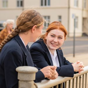 2 students leaning against a fence