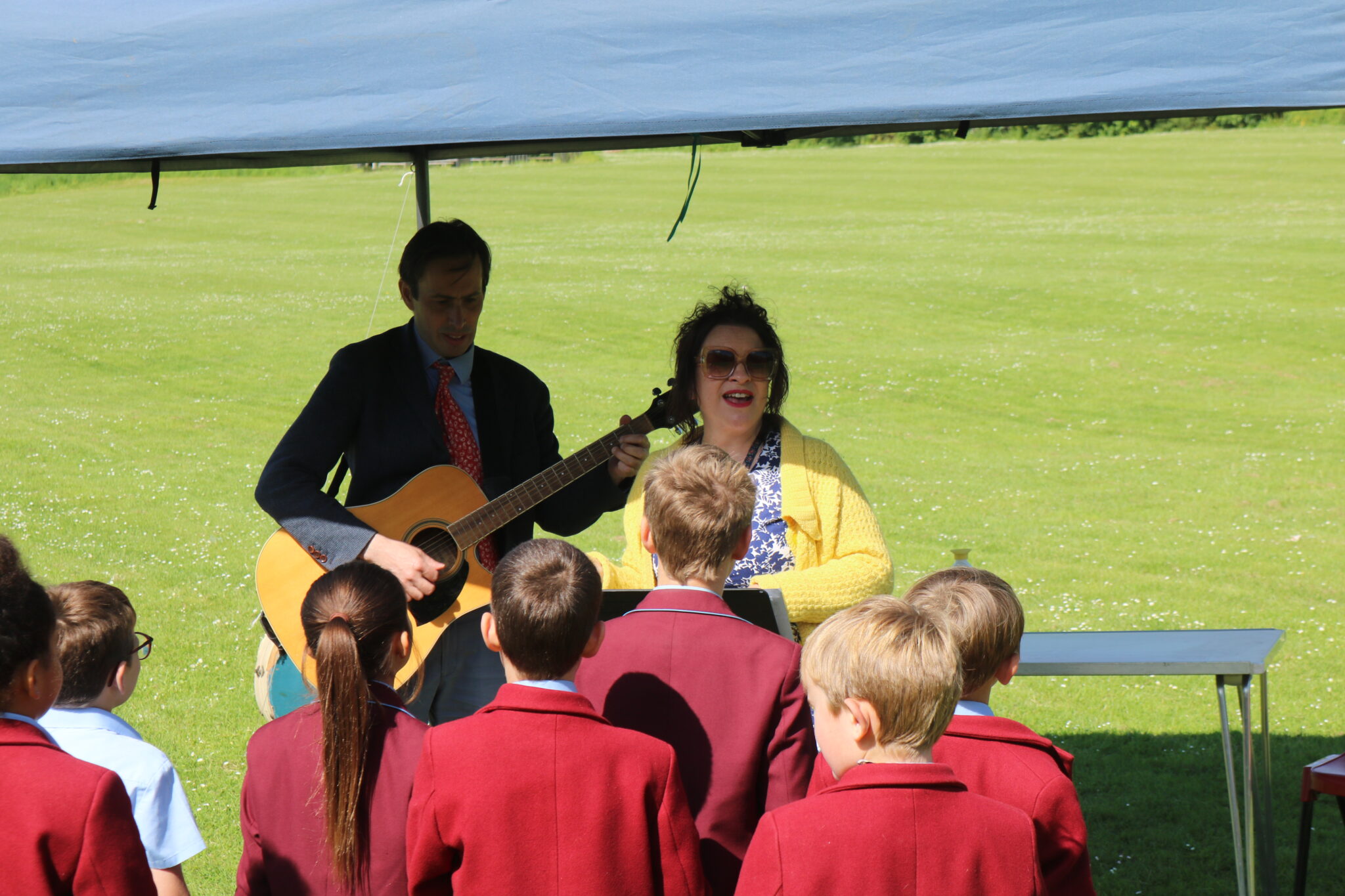 Children in red blazers singing with teacher with guitar